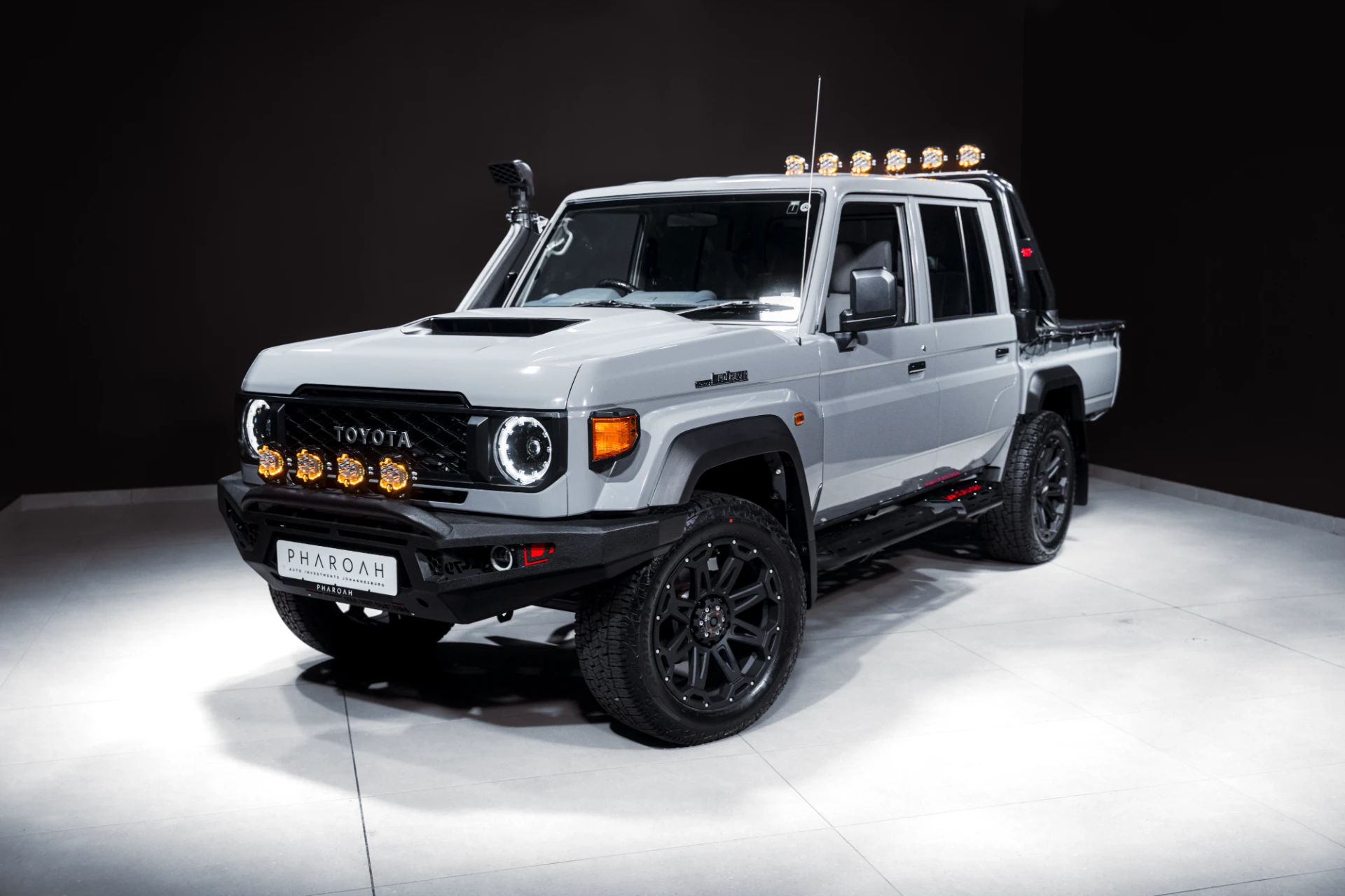 White Toyota off-road truck on showroom floor with multiple amber roof and bumper lights, glossy finish.