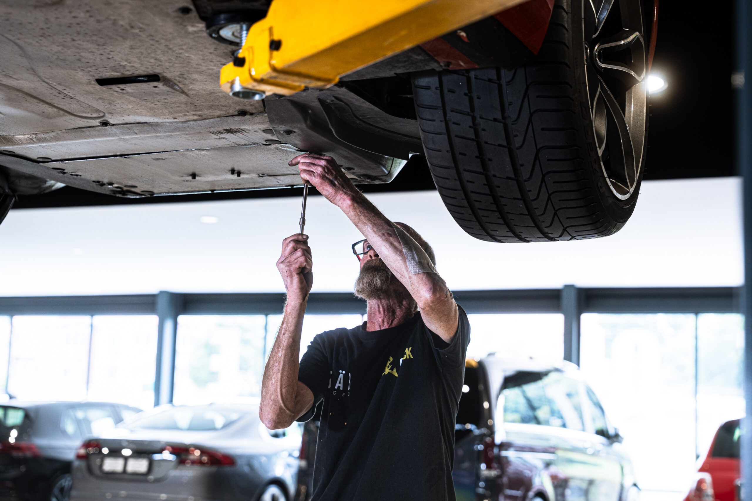 Mechanic using a wrench under a raised orange car on a hydraulic lift in a bright workshop