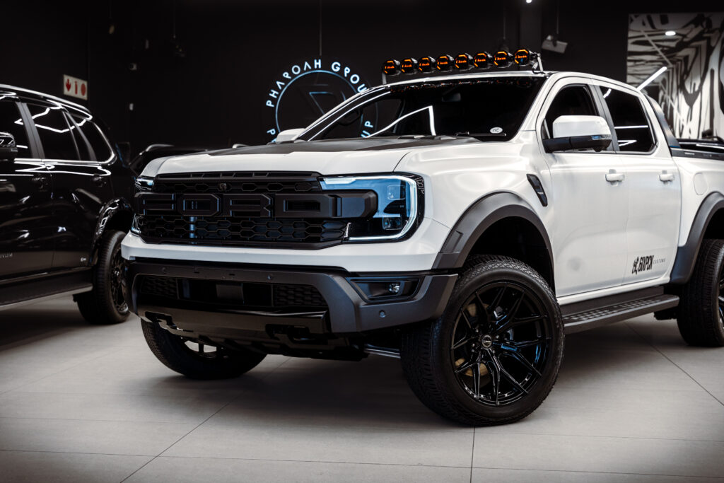 White pickup truck with a bold black grille and rooftop orange light bar displayed in a showroom environment