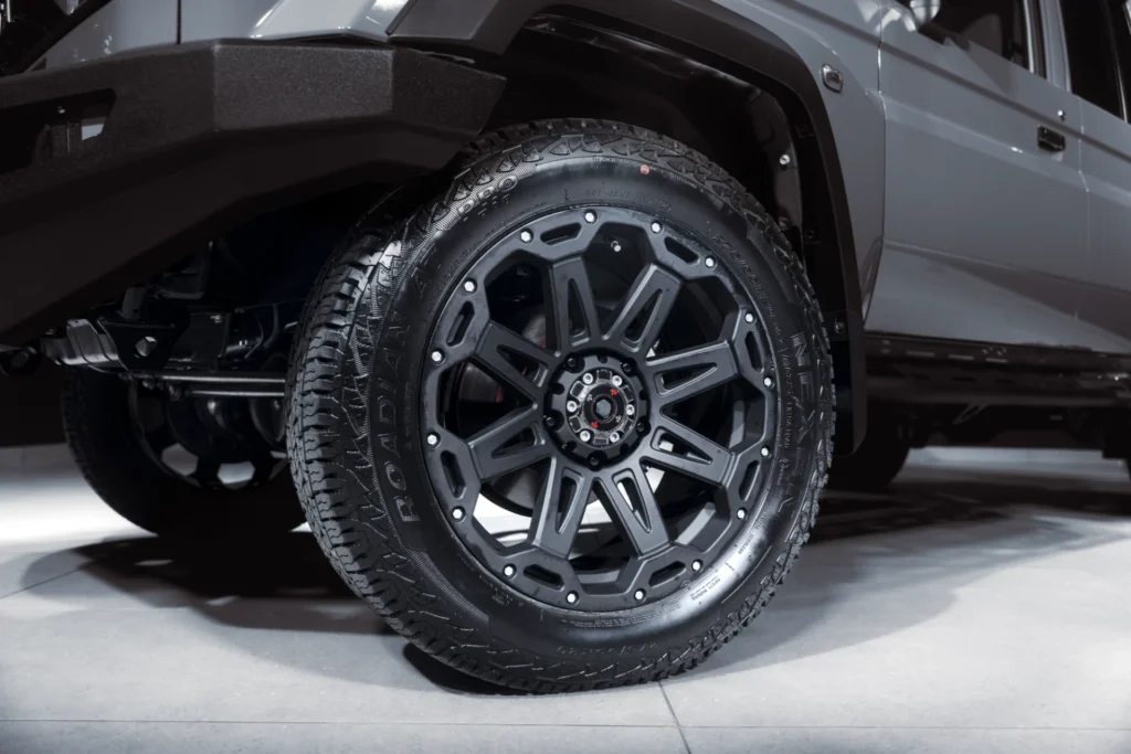Close-up of a rugged all-terrain tire mounted on a dark gray multi-spoke alloy wheel, with the wheel well and vehicle body visible, indoors.