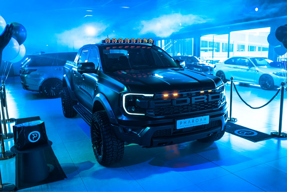 Black lifted Ford pickup on a blue-lit showroom floor with other cars in the background.