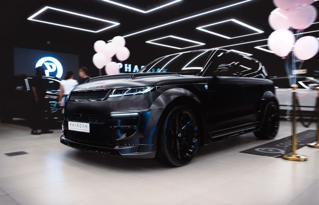 Front three-quarter view of a glossy black SUV displayed in a showroom with bright geometric ceiling lights and pink balloons in the background.