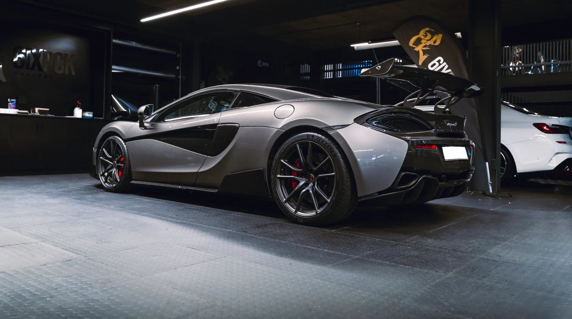 Silver McLaren supercar with a large rear wing on display in a dim showroom showroom setting