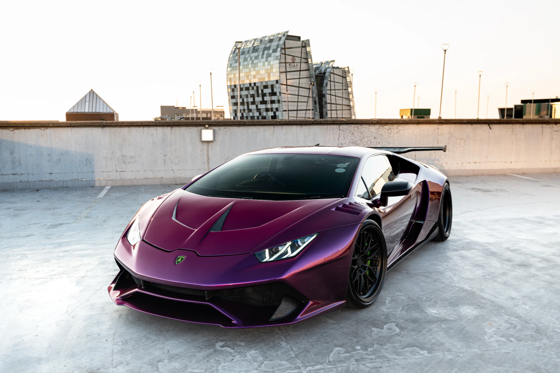 Purple Lamborghini sports car parked on a rooftop with modern glass buildings in the background