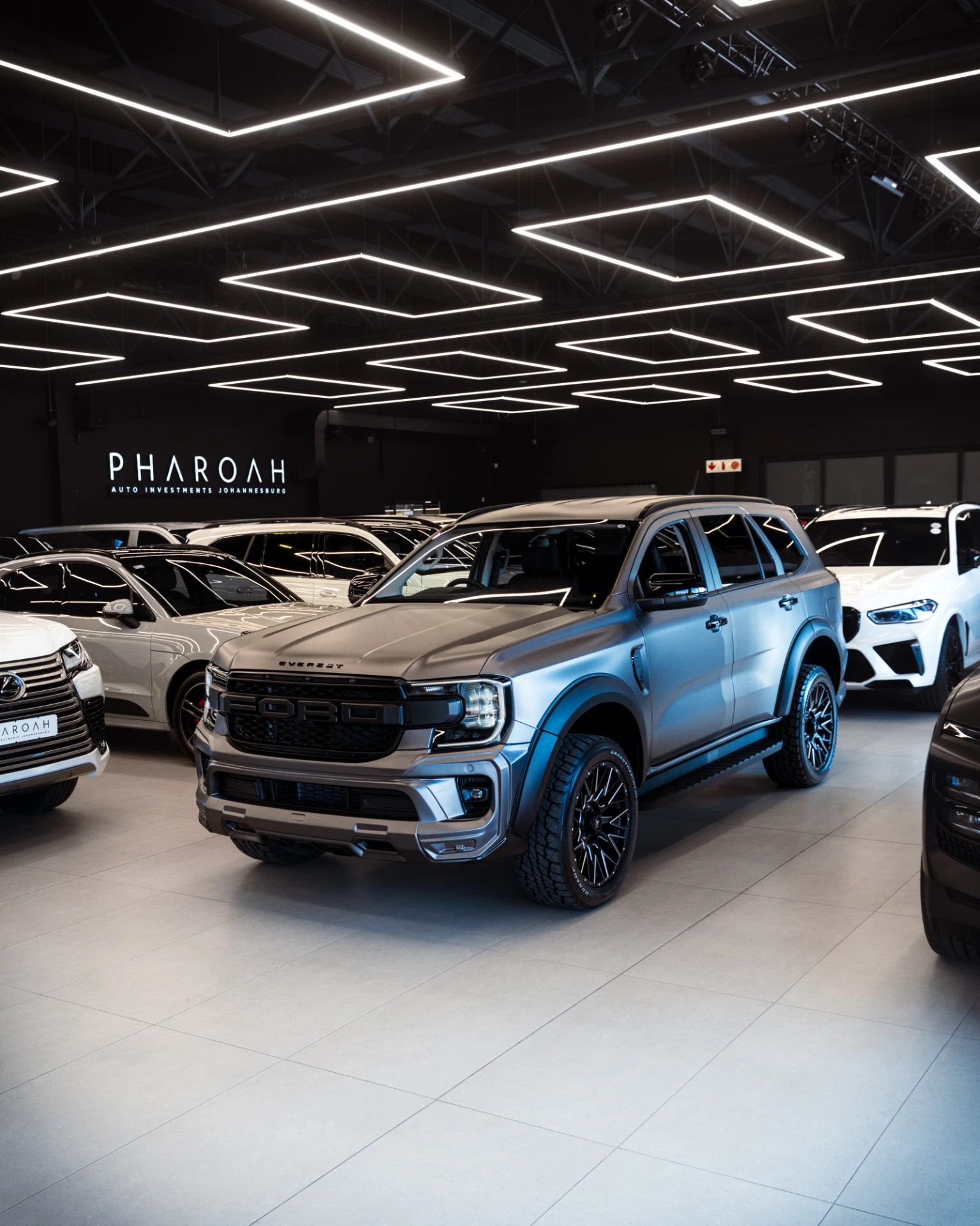 Blue pickup truck in a showroom with other vehicles and geometric square LED lights overhead, creating a modern display.”,