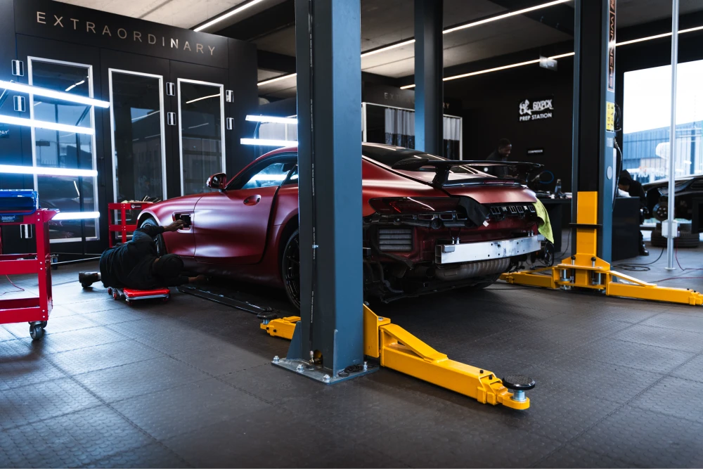 Red sports car on a hydraulic lift in a modern workshop, mechanic working underneath it on a creeper.